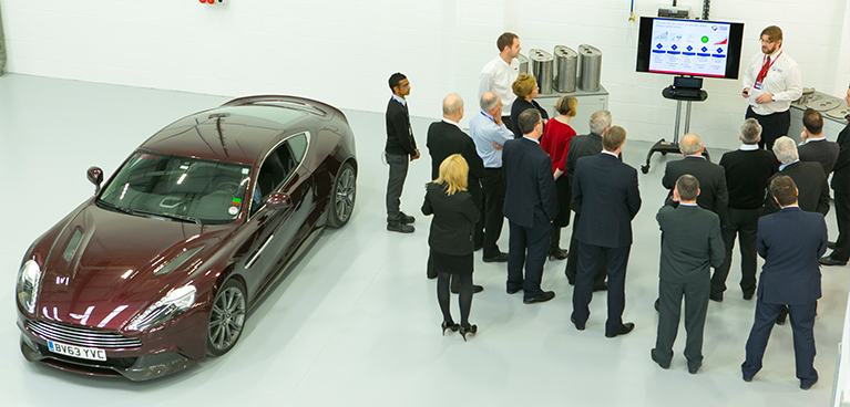 People in suits watching a presentation next to a sleek new car.
