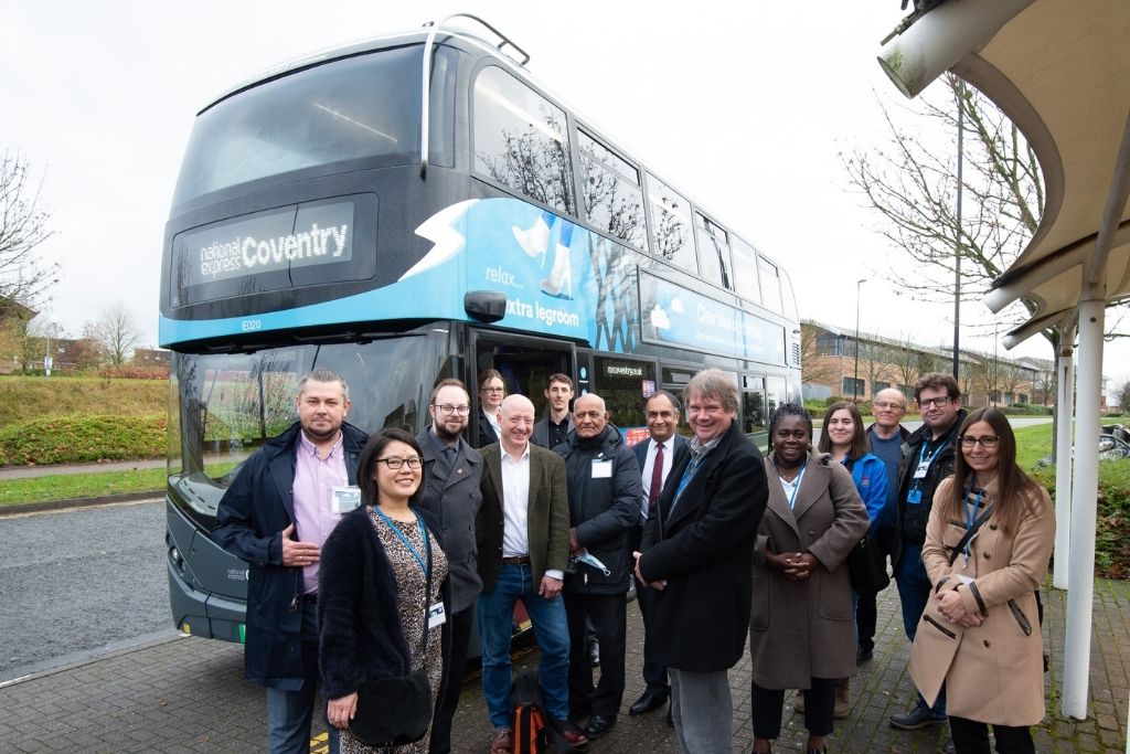 A group of 15 people stand next to an electric powered bus