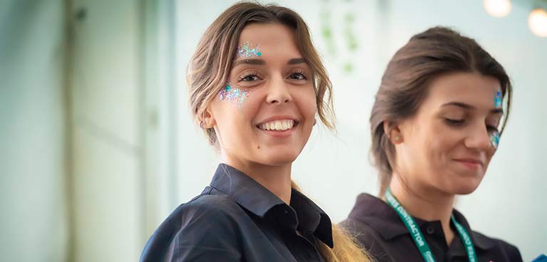 Two females one girl with glitter on here face looking directly at the camera smiling