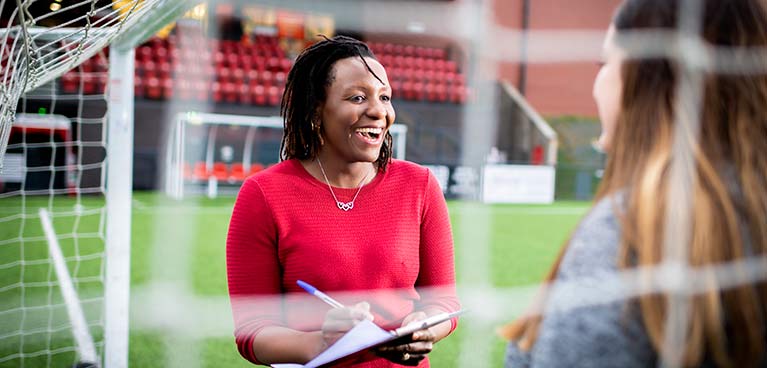 Girl holding a clip board and pen on a sports pitch 