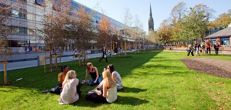 Group of 5 students sitting on green space 