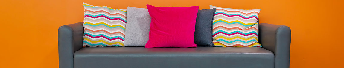 Black leather sofa with cushions against a bright orange wall