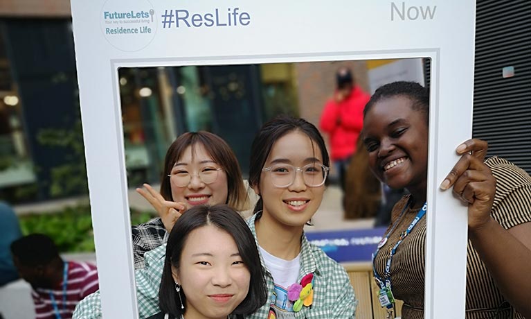 Students holding up a Coventry University Halls of Residence selfie frame and smiling.