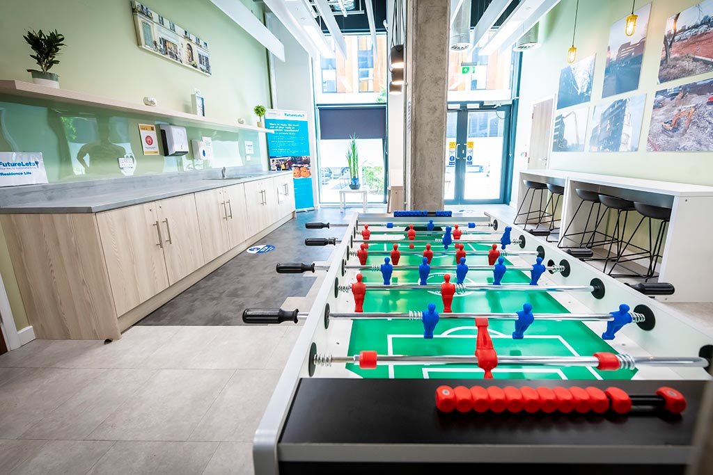 Table football in an open room with tables and chair opposite glass doors