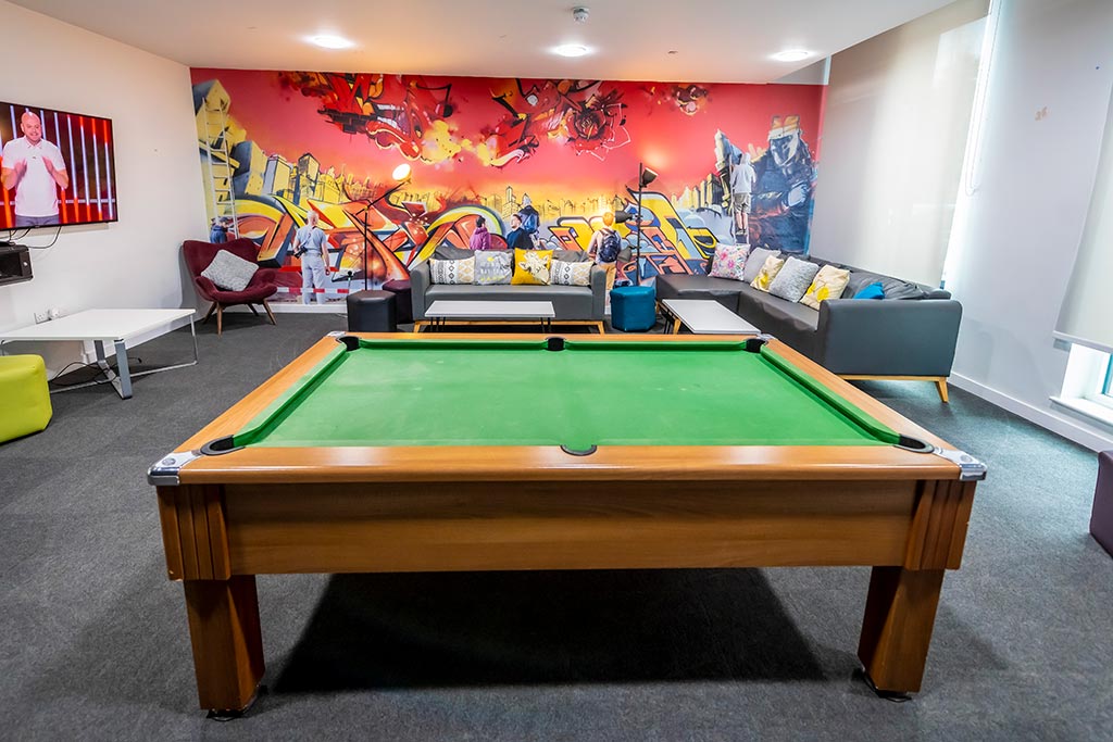 Pool table in a room with a graffiti art feature wall with sofa's and tv mounted to the wall