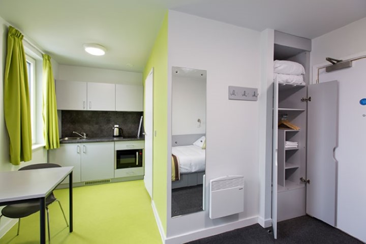 Premium studio with lime green soft furnishings, kitchen and dining area and an open cupboard