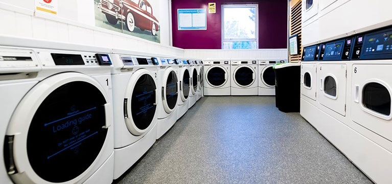 Laundrette in Singer Hall, with a long row of washing machines and a double row of tumble dryers.