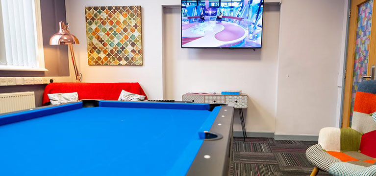 A social space in Singer hall with a wall-mounted tv screen, comfortable seating and a pool table.