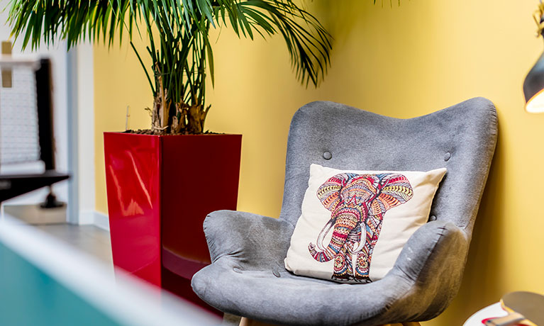 Grey chair against a yellow wall with a cushion with an elephant print on