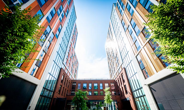 Outside view of a tall accommodation block with bright coloured cladding and trees