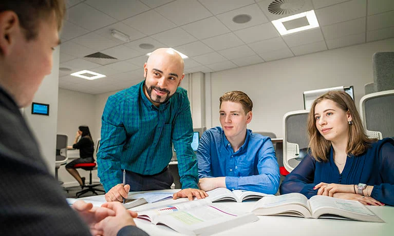 Lecturer standing at a table speaking to three students