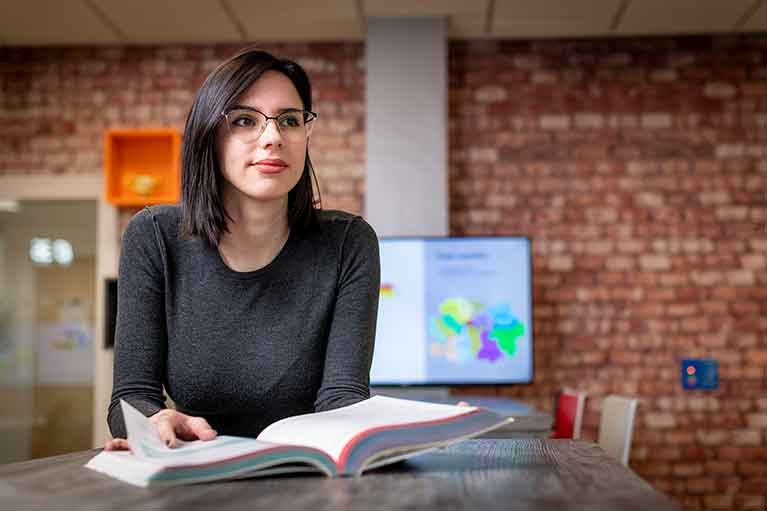 A student sitting at a table in the DigiComm Lab reading a book