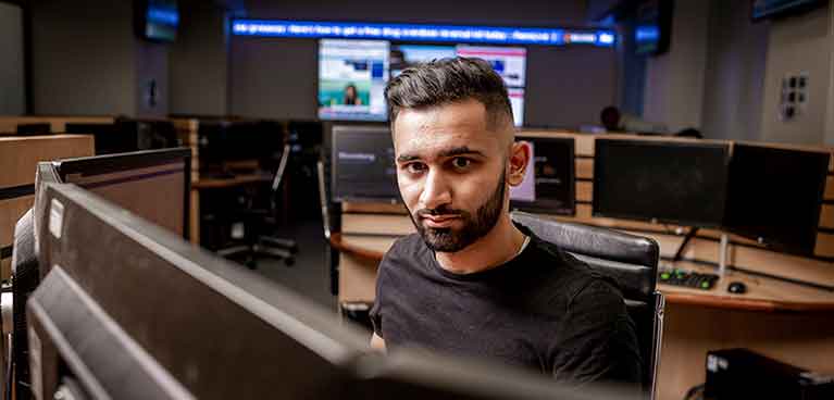 man looks at camera, screen in front of him, screens behind him