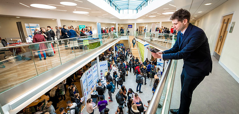 A smartly dressed man leans on a railing with a busy atrium below