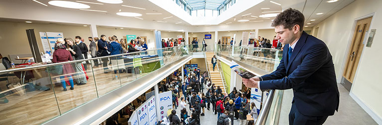 A man is leaning on a banister overlooking an atrium filled with people