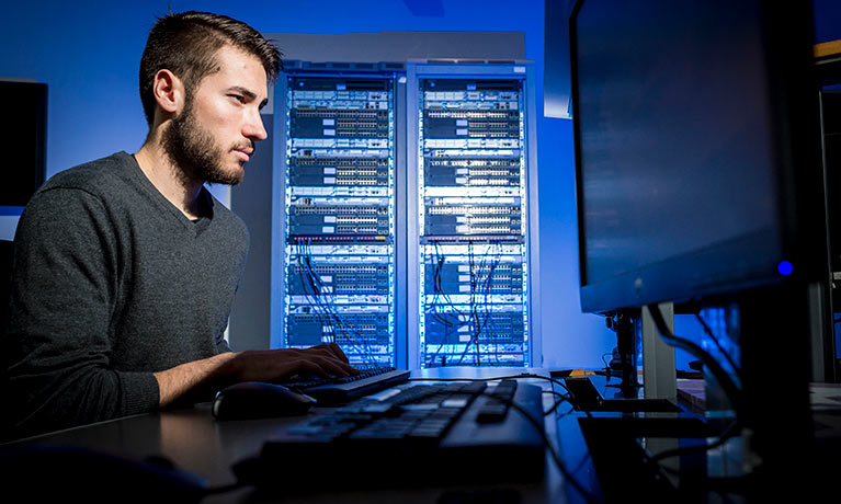 Male student working at a computer having server racks on the background