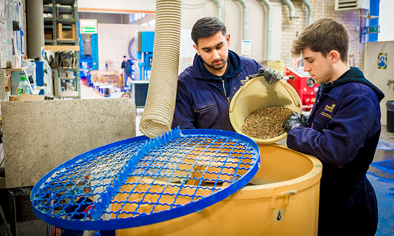 Two male students pouring materials into a machine.