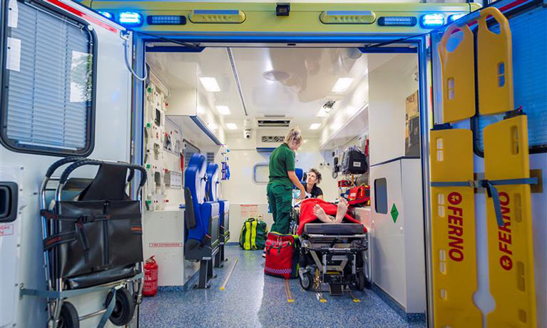 Inside a mock ambulance with the doors and a parademic and doctor working on a mock patient on a stretcher