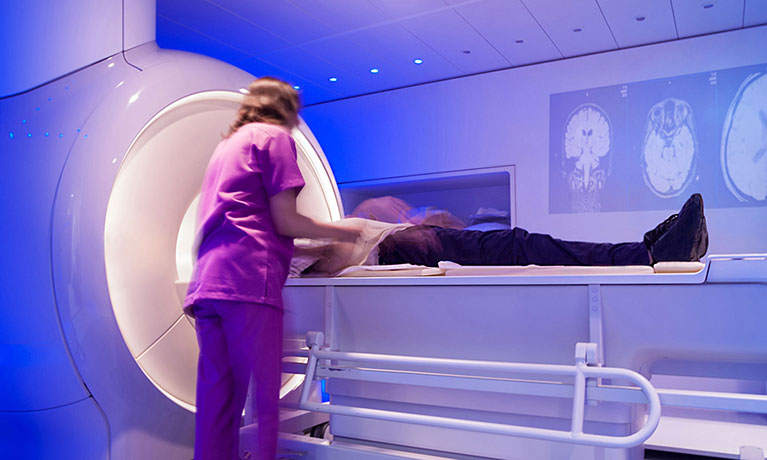 Radiography suite, a staff member helps a patient in a machine
