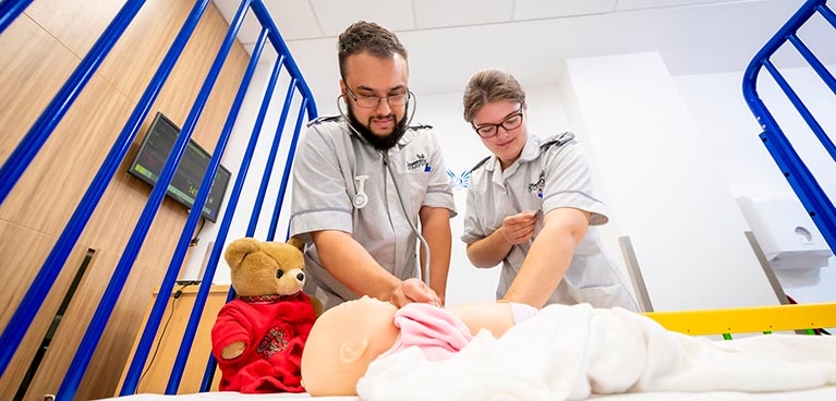 Nurses looking down on a bed with a dummy baby in it