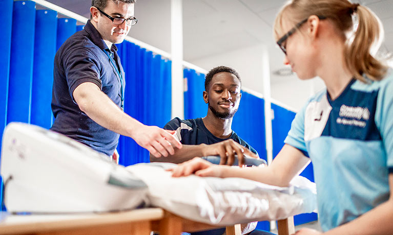 Two male students checking a female students arm