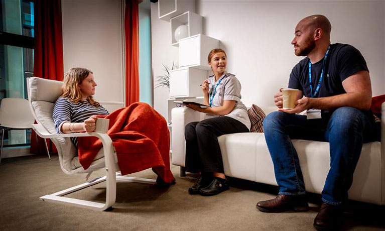 Male and female students talking a female who is sitting down with a drink