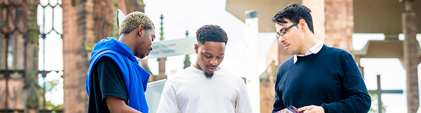 Three students stood by the cathedral looking at something on a phone