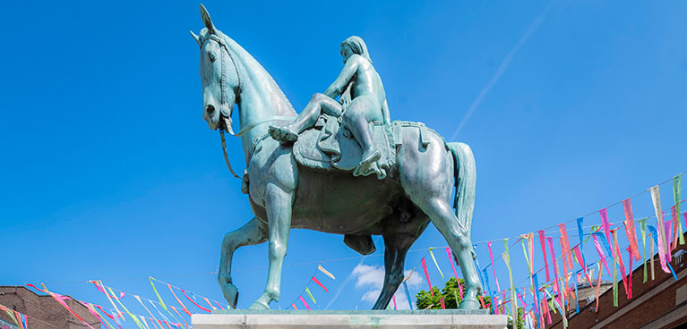 Lady Godiva statue on sunny day with colourful ribbons in the background