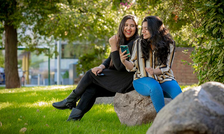 Two young adults sitting on a bench and looking at a smartphone