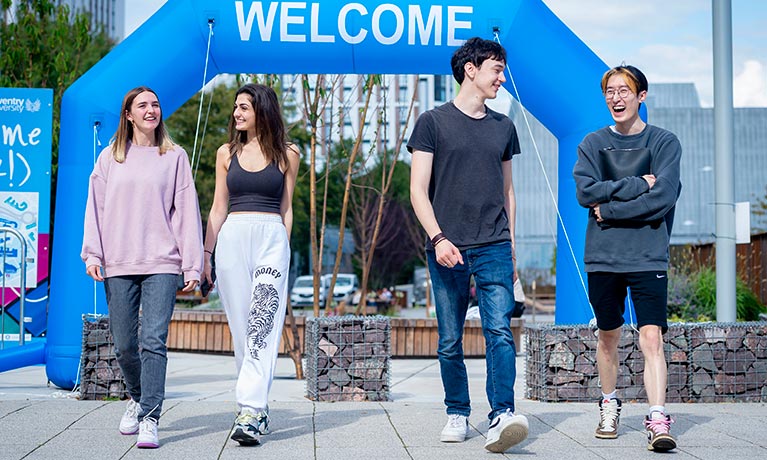 two female and two male students walking through campus whilst talking and laughing