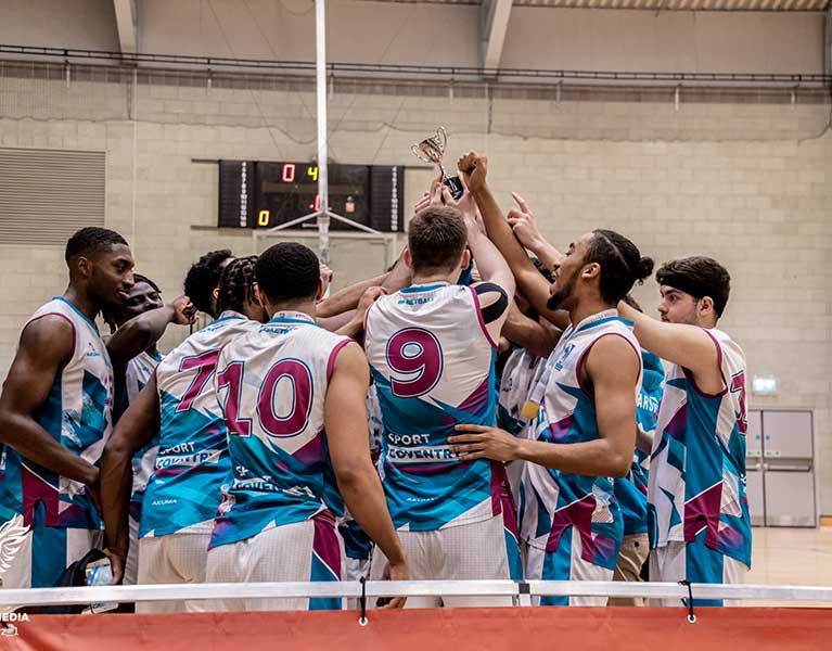 A Coventry University basketball team celebrating a win by holding a trophy in the air