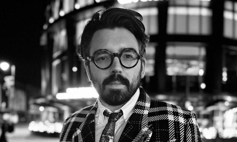 Joshua looking into the camera, standing infront of a city building