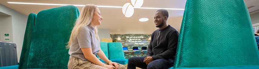 Blonde woman and brunette man chatting while sitting on big green velvet armchairs