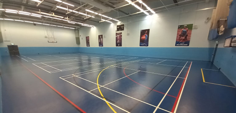 A large sports hall, empty of visitors. Clear line-marking on floor.