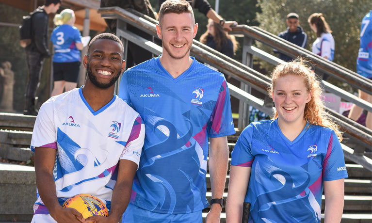 Three students smiling in sports kit.