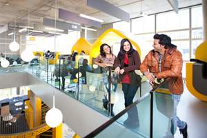 Some students leaning on a glass banister on campus laughing with each other