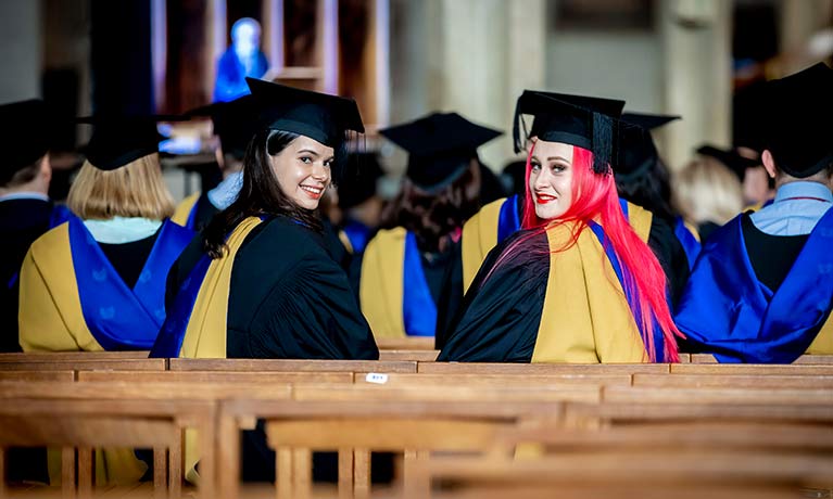 Two female students looking behind them sitting in Coventry Catherdral 