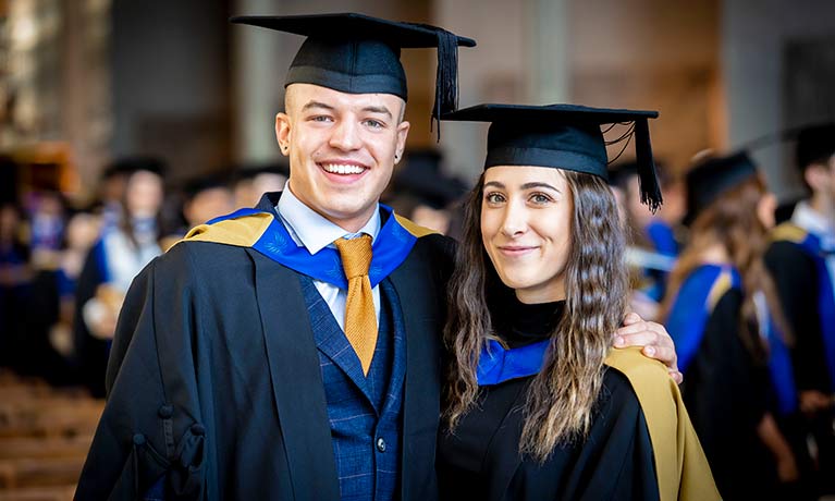 Male and female students smiling looking at camera wearing gown and hats