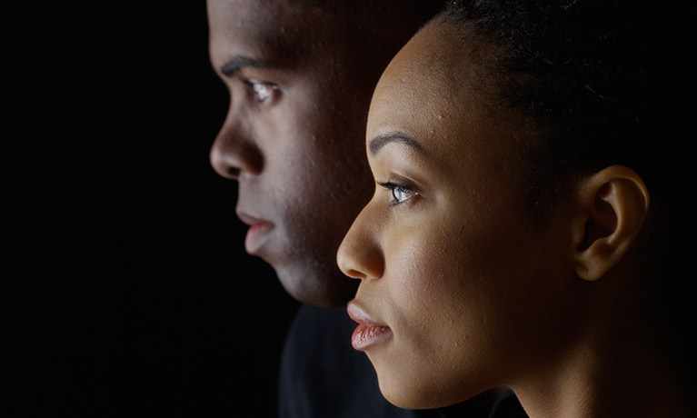 A Black man and woman look left in front of a black background