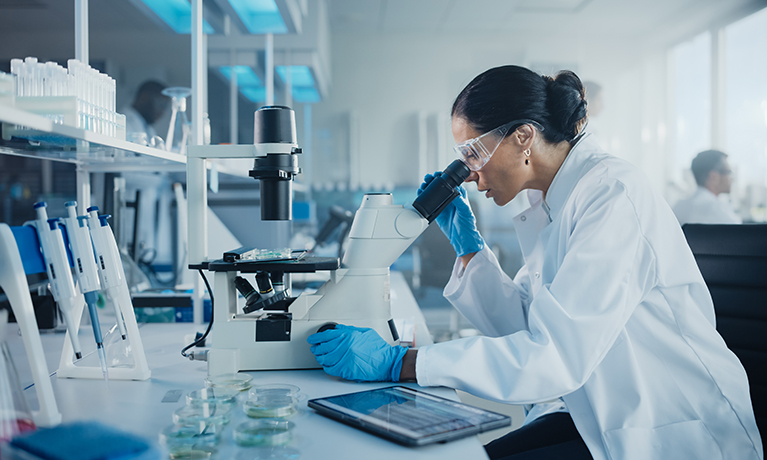 women in lab wearing a lab coat looking into a microscope