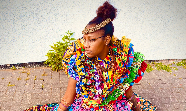 A woman sits on the pavement wearing a colourful dress