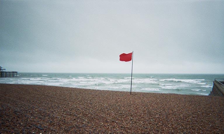 Red flag poled on a beach in a windy day