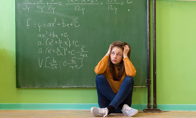 Student on the classroom floor in frustration in front of a blackboard with maths