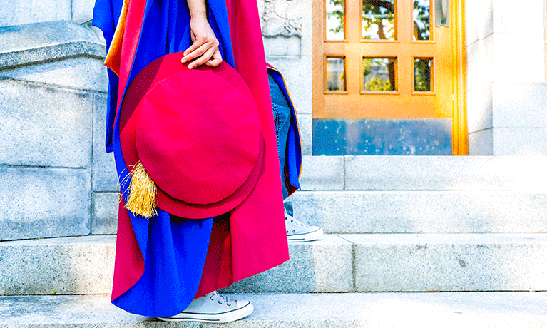 A PhD graduate holding their cap climbing stairs