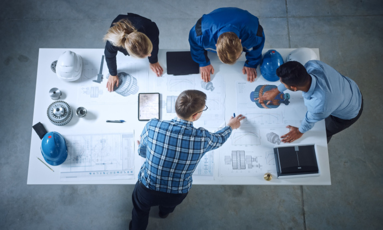 Team of industrial engineers lean on office table, analyse machinery blueprints, architectural problem solving, consult project on tablet computer, inspect metal component. Flat lay top down view