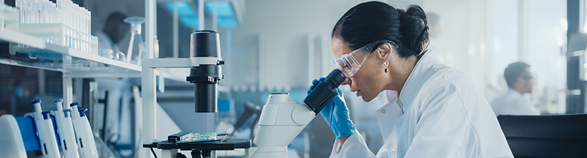 woman in a lab wearing a lab coat looking into a microscope