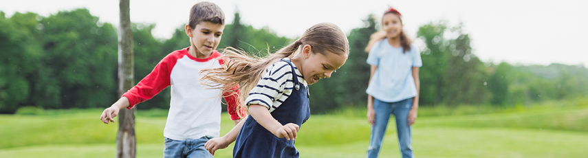 Two little girls and one little boy playing in a field on a sunny day.