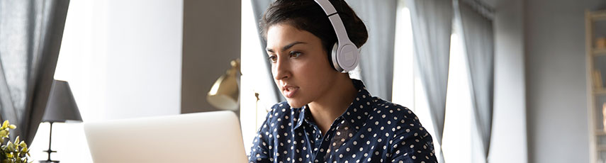 a woman sits at a laptop wearing headphones