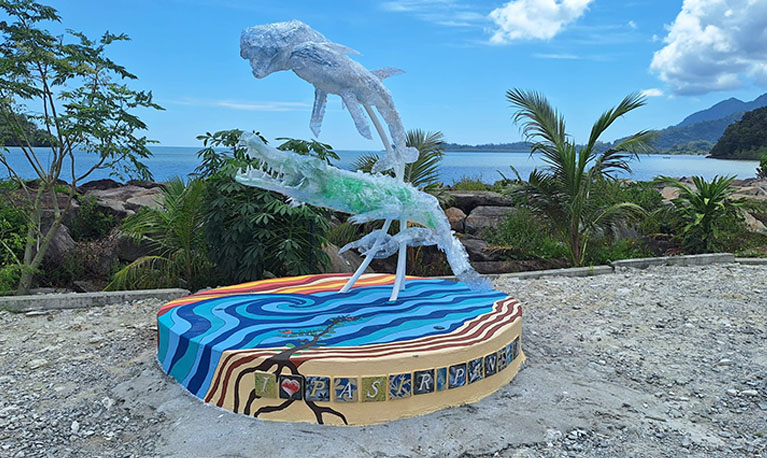 sculpture of whale and crocodile in front of the ocean with palm trees