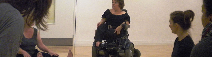 Dancer in a wheelchair with other dancers sat on the floor